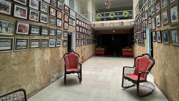 Un hall d’entrée spacieux, doté d’un haut plafond et d’une verrière, avec un mur orné de photos encadrées et deux fauteuils rouges placés au centre.
