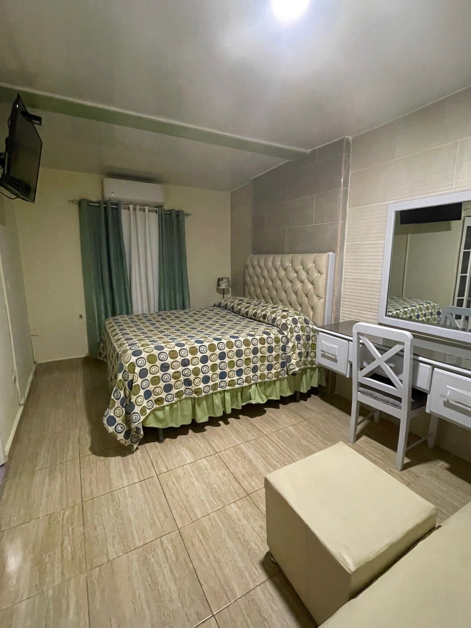 Een slaapkamer met een bed, een bureau, een stoel, een spiegel en een televisie die aan de muur bevestigd is.
