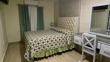 A bedroom with a bed, a desk, a chair, a mirror, and a TV mounted on the wall.