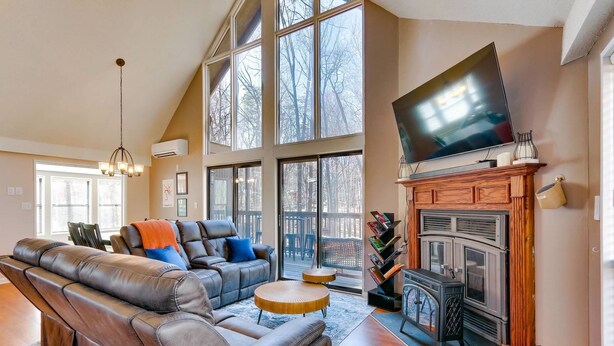 A spacious living room with a large sectional sofa, a fireplace, a flat-screen TV, and a large window offering a view of the outdoors.