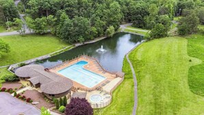 A large swimming pool with a hot tub, surrounded by a well-maintained lawn and a pond.