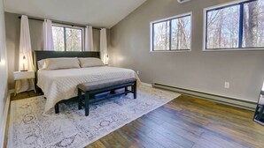A bedroom with a bed, bedside tables, a bench, a rug, and large windows with a view of trees.