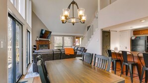A spacious dining area with a large wooden table and black chairs, a chandelier, and a view of the outside through large windows.