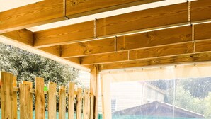 A wooden deck with a table and chairs, a wooden fence, and a view of a building through a window. - Between sea and forest 2 near the beaches (Jard-sur-Mer)