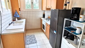 A compact kitchen with a sink, stove, refrigerator, and wooden cabinets. - Between sea and forest 2 near the beaches (Jard-sur-Mer)