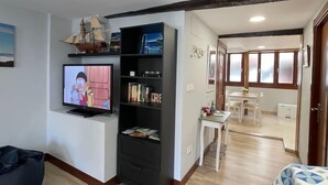 Een woonkamer met een televisie, een boekenkast en een eethoek met een tafel en stoelen.