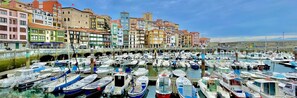 Un puerto deportivo con numerosas embarcaciones amarradas, rodeado de edificios coloridos y un puente de piedra.