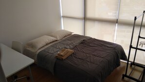 A bedroom with a bed, a desk, and a window.