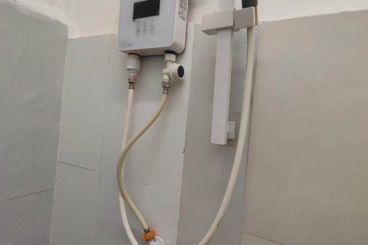 Un baño con paredes de azulejos, un cuadro eléctrico blanco y dos tuberías conectadas a él.
