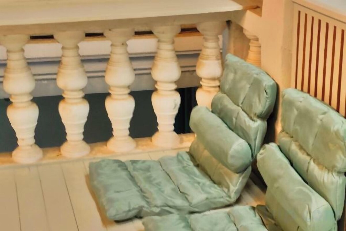 A section of a room with a white balustrade and a row of green upholstered chairs.