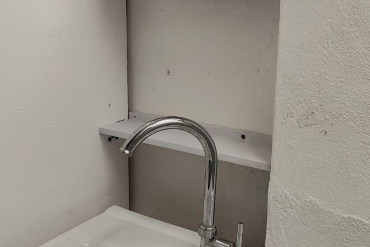 Un baño pequeño y blanco con un lavamanos y un grifo cromado.