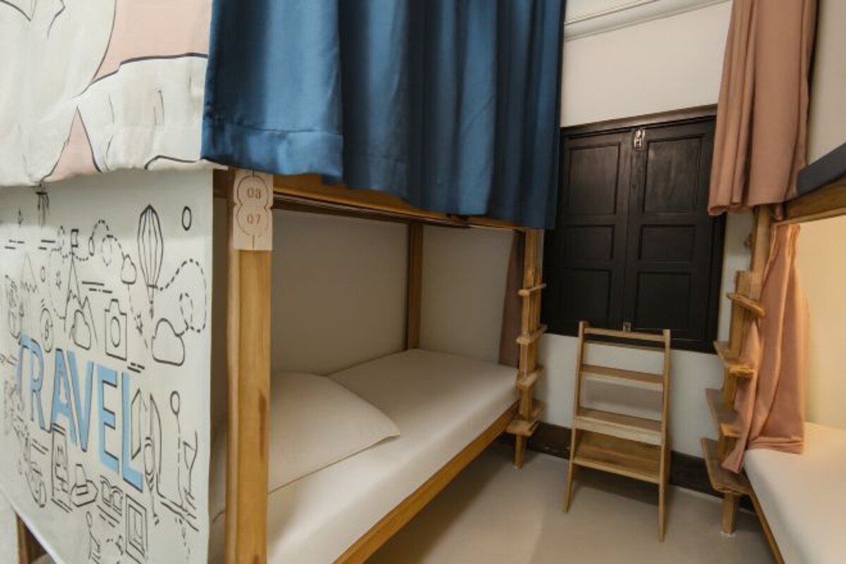 Habitación con literas, una cortina azul, escalera de madera y un mural con motivos de viaje.