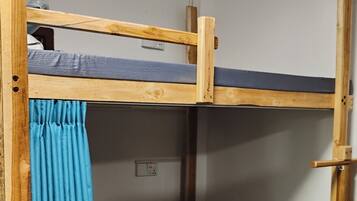 A bunk bed with a blue curtain, a wooden ladder, and a power outlet on the wall.