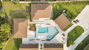 Vista aérea de uma casa moderna com piscina, vários quartos e um gramado bem cuidado.