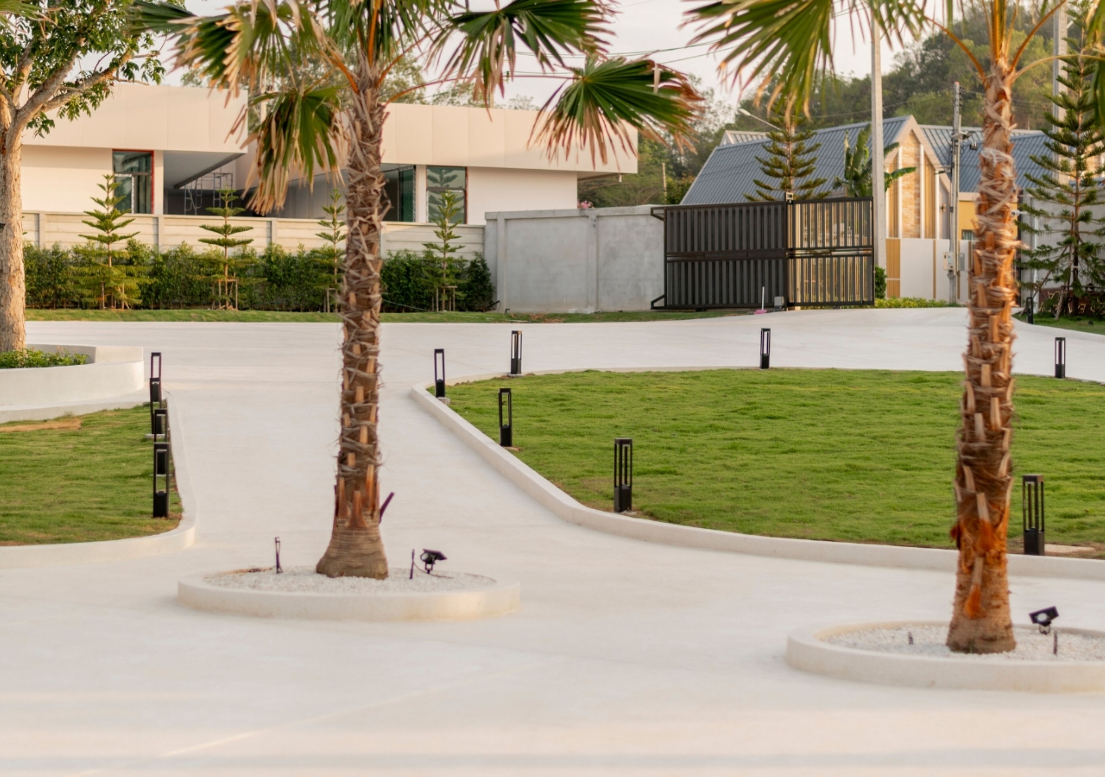 A modern outdoor area with palm trees, a paved walkway, and a gated entrance.