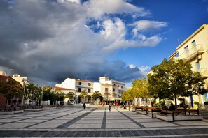 A spacious public square with benches and trees, surrounded by buildings with balconies and architectural details.