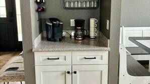Una cocina con armarios blancos, cafetera y nevera para vino.