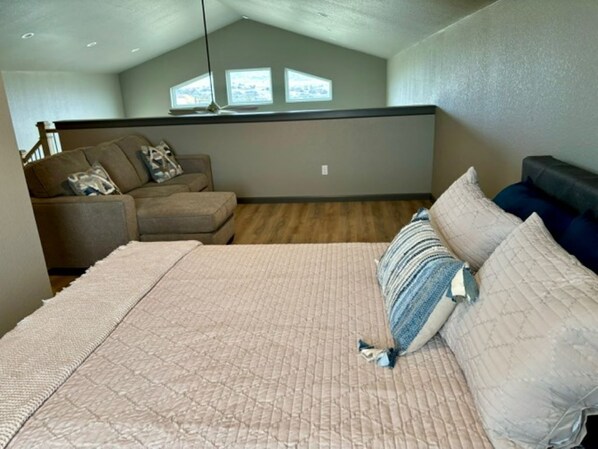 A bedroom with a large bed, a sofa, and a view of the outdoors through a window.