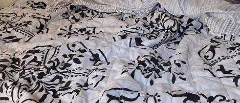 A bed with a white and black floral patterned duvet and striped pillows.
