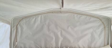 A compact travel bed with a mattress and headboard, a small table, and a power outlet.