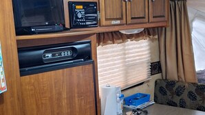 Ein kompaktes Wohnmobil-Interieur mit Holzausbau, einem festinstallierten Fernseher, einer kleinen Küchenzeile und einer Sitzecke mit gemusterten Kissen.