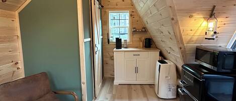 A cozy attic bedroom with a sloped ceiling, wooden walls, a window, a bed, a chair, and a small table with a plant.