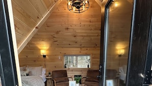 L’intérieur d’un chalet en bois chaleureux et accueillant, avec un lit, deux canapés, une table basse et un lustre.
