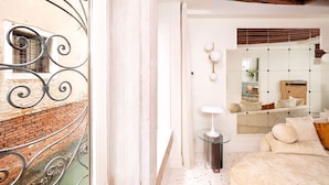 A modern bedroom with a large bed, a glass side table, a mirror, and a view of a brick building outside. - Charming Canal View Apartment in Idyllic Location (Venecia)