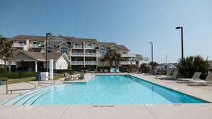 A swimming pool with a 'NO DIVING' sign, surrounded by lounge chairs and a building with balconies. - New! Condo with Dock + Pool (Carolina Beach)