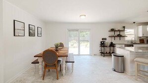A spacious kitchen with a dining area, featuring a marble floor, wooden furniture, and a view through a glass door. - New! Game Room + Close to Beach (Wilmington)