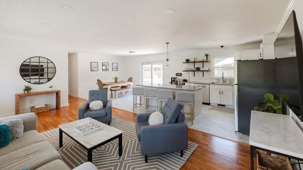 A modern living room with a sofa, armchairs, and a coffee table. There is a kitchen area with white cabinets and a refrigerator. - New! Game Room + Close to Beach (Wilmington)