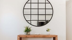 A wooden console table with two potted plants, a mirror with a black grid frame, and a power outlet on the wall. - New! Game Room + Close to Beach (Wilmington)