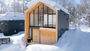 A modern cabin with large windows, a wooden door, and a snow-covered roof. - Kouzan Woods (Niseko)