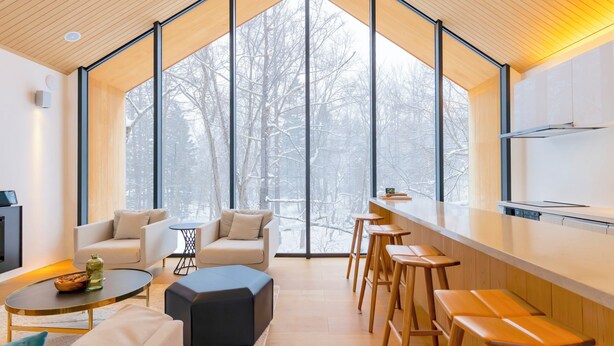 A modern interior with a large window, a kitchen area, and seating arrangements. - Kouzan Woods (Niseko)