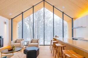 A modern interior with a large window, a kitchen area, and seating arrangements. - Kouzan Woods (Niseko)