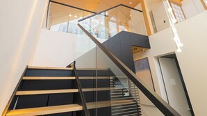 A modern interior with a wooden staircase, glass railings, and a ceiling with hanging lights. - Kouzan Woods (Niseko)