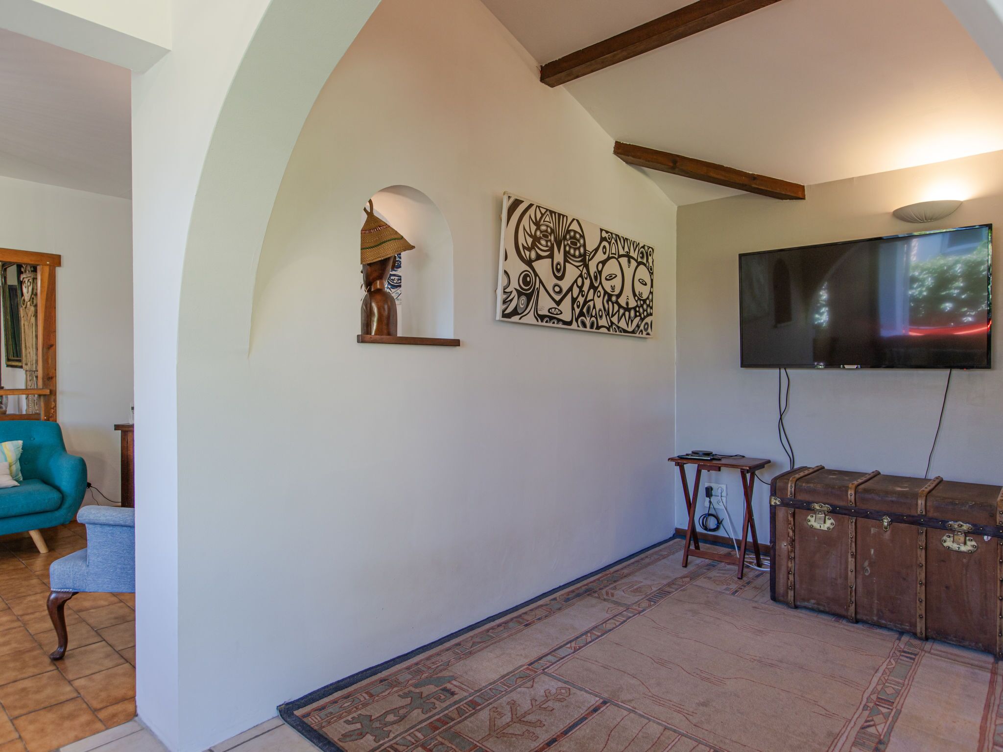 A living room with a television mounted on the wall, a wooden cabinet, a blue sofa, and a patterned rug.