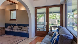 A cozy living room with a sofa, a coffee table, and a dining table. There is a large window providing a view of the backyard.