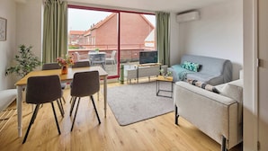 A modern living room with a sofa, a dining table with chairs, a TV, and a large sliding glass door leading to a balcony. - Nimma Voorstad Stay Nijmegen (Nijmegen)