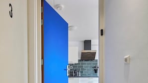 A hallway leading to a kitchen with white cabinets, a blue door, and a brown doormat. - Nimma Voorstad Stay Nijmegen (Nijmegen)
