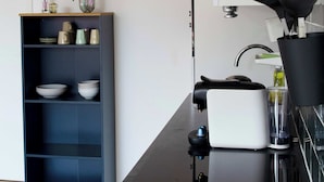 A modern kitchen with a clock, shelves with dishes, and a coffee maker. - Nimma Voorstad Stay Nijmegen (Nijmegen)