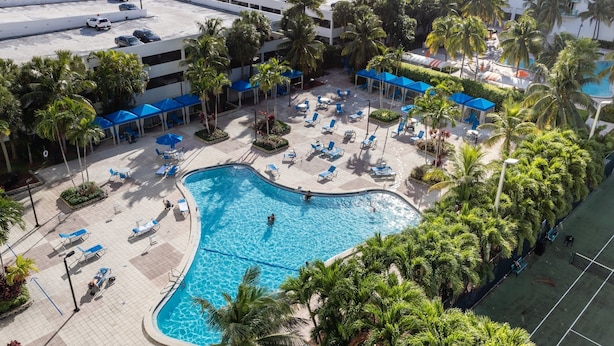 A pool area with lounge chairs and umbrellas, surrounded by palm trees and a building in the background. - Awesome Miami Sunny Isles Ocean Reserve Condo (Sunny Isles Beach)