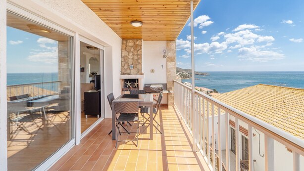 A balcony with a wooden ceiling, a stone wall, and a view of the sea.