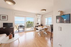 Enjoy a sea view from the large window in this stylish living area, featuring a flat-screen TV, dining table, and decorative artwork.