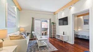 Una sala moderna con sofá, mesa de centro y televisor. Tiene un balcón con barandilla y vistas a un edificio.