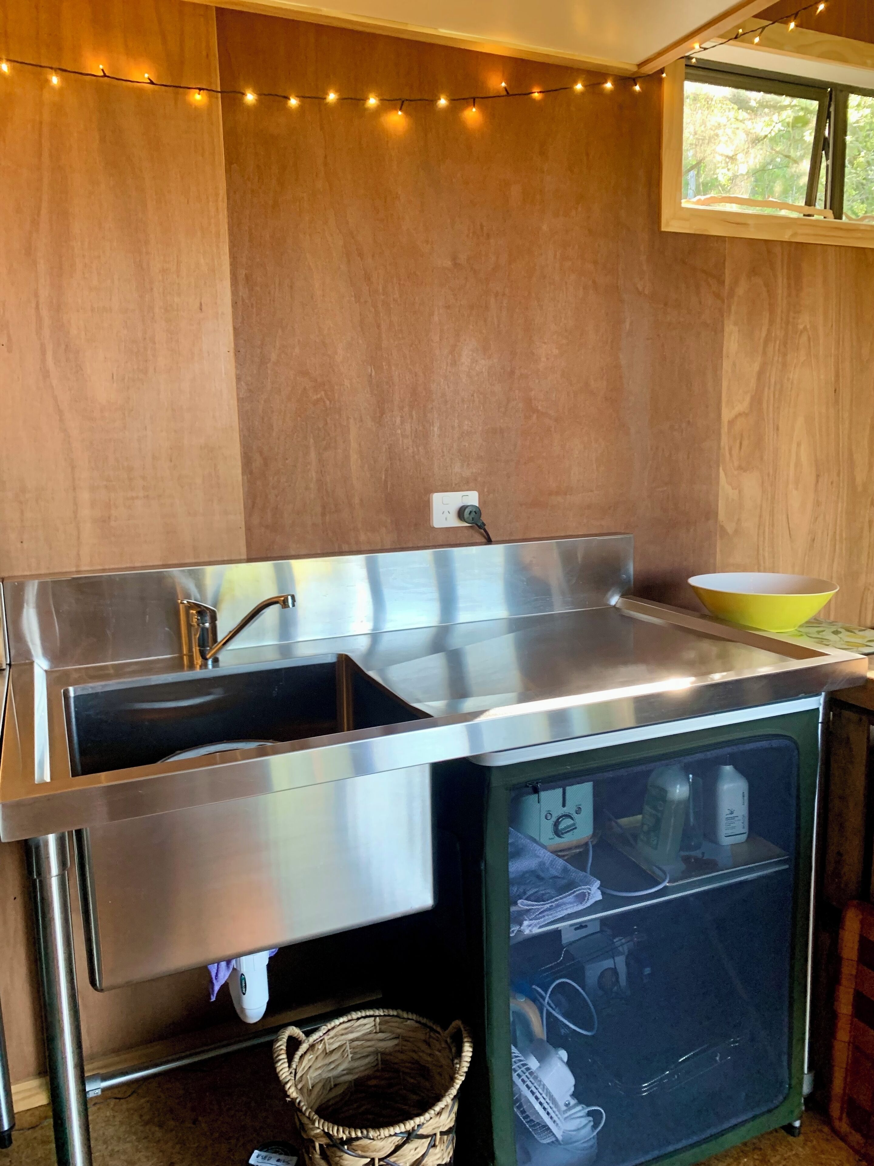 Una cocina con un lavamanos de acero inoxidable, un tazón amarillo y una ventana con vistas a árboles.