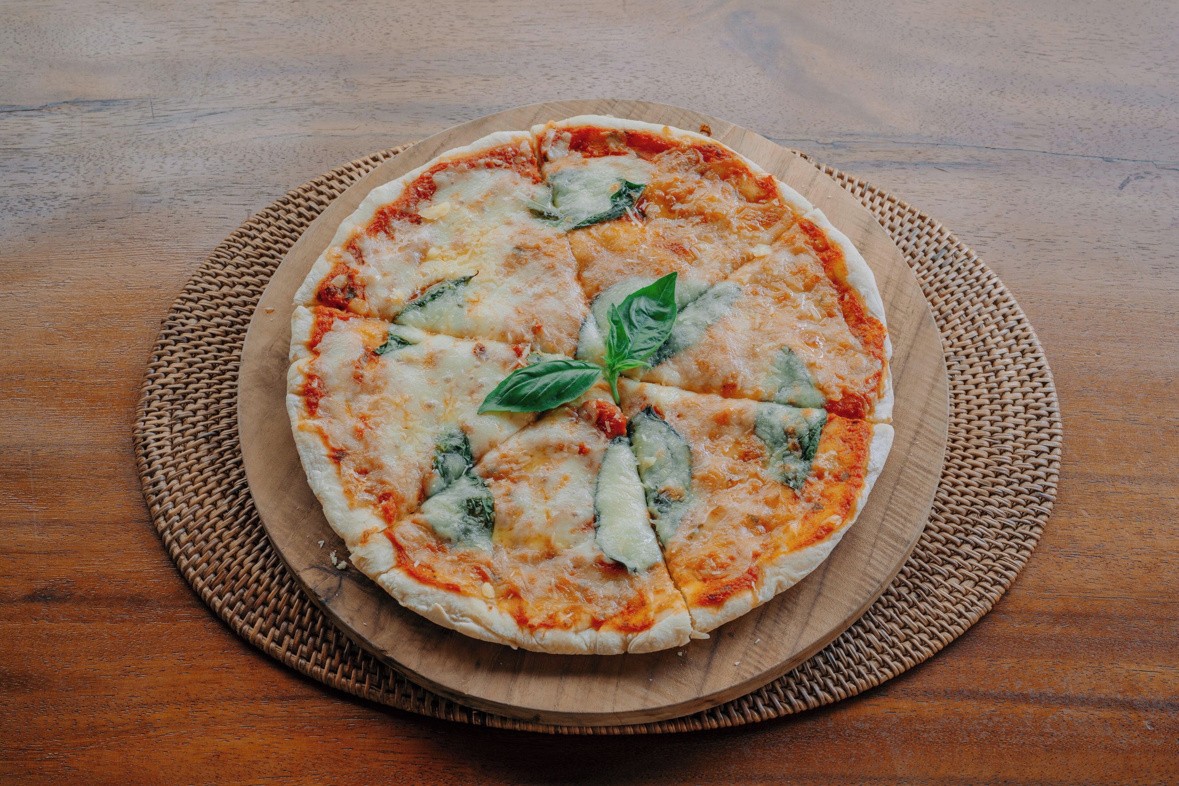 Une pizza servie sur une planche en bois, posée sur un tapis tressé.