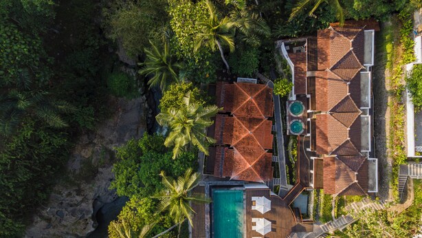 Luchtbeeld van een resort met een zwembad, meerdere bungalowachtige gebouwen en weelderige tropische begroeiing.