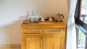Een houten kastje met glazen potten en een koffiezetapparaat erop, geplaatst naast een raam met witte gordijnen.