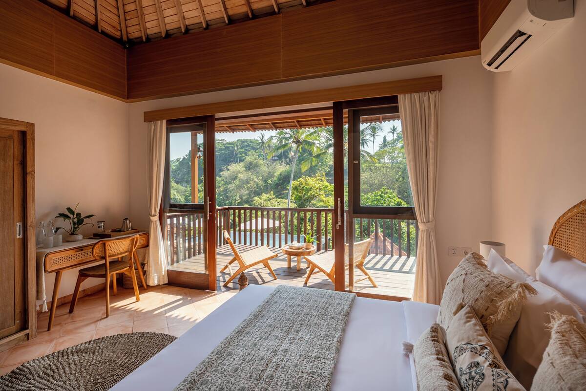 A bedroom with a large bed, a desk, and a balcony with chairs and a table.